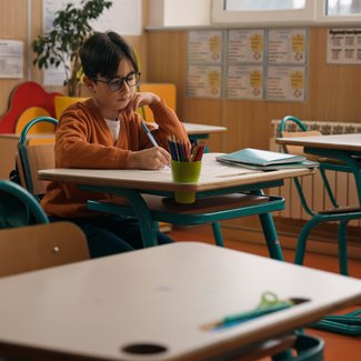 Ein Junge sitzt alleine in einem Klassenzimmer und schreibt.