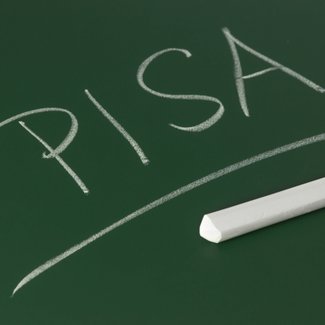 An einer Tafel ist mit Kreide das Wort Pisa geschrieben. Darunter liegt eine Tafelkreide.