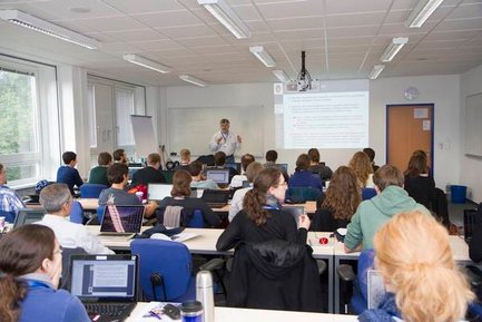 [Translate to English:] A person stands in front of an audience and gives a presentation.