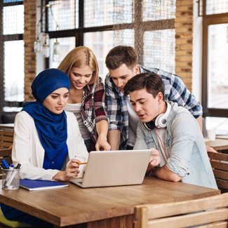 Eine diverse Gruppe von Studierenden arbeiten gemeinsam an einem Laptop.