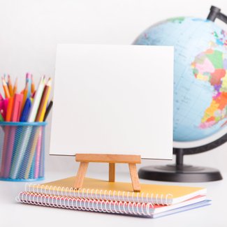 Eine kleine weiße Leinwand, die auf einem Notizblock steht. Im Hintergrund sind Buntstifte und ein Globus zu sehen.